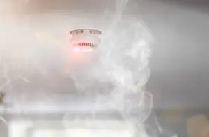Smoke alarm activating with visible smoke in the room, signaling potential fire.