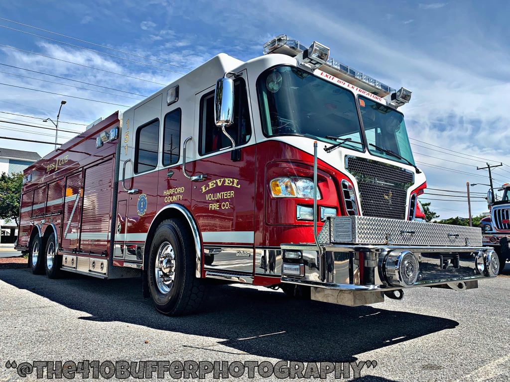 A red and white fire truck with "Level Volunteer Fire Co." and "Harford County" painted on the side is parked on a paved area. The sky is clear with a few clouds. Photo credit is given to "The110BufferPhotography.