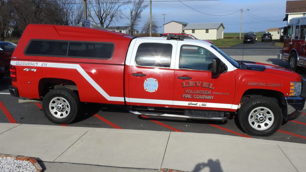 A red and white Level Volunteer Fire Company truck is parked outside on a street. The vehicle is marked with emergency labels and is equipped for off-road terrain.