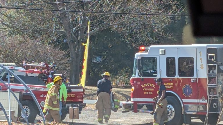 Firefighters dressed in gear stand near a Harford County fire truck labeled "Level Volunteer Fire Co." They are gathered in an outdoor area with trees in the background, engaged in a safety briefing or preparation.